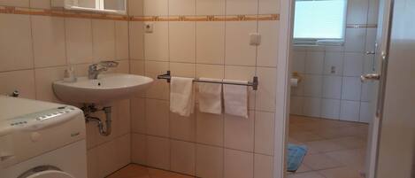 A small bathroom with a sink, a mirror, a towel rack, and a washing machine.