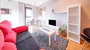 Moderni olohuone, jossa on sohva, sohvapöytä, televisio ja kirjahylly.