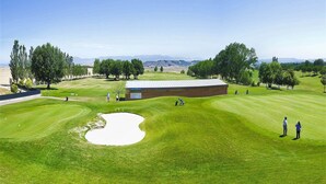 Golfkenttä, jossa on hiekkabunkkereita, puita ja klubitalo.