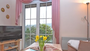 Un salon avec un téléviseur, une table ornée d’un vase de fleurs et un canapé.