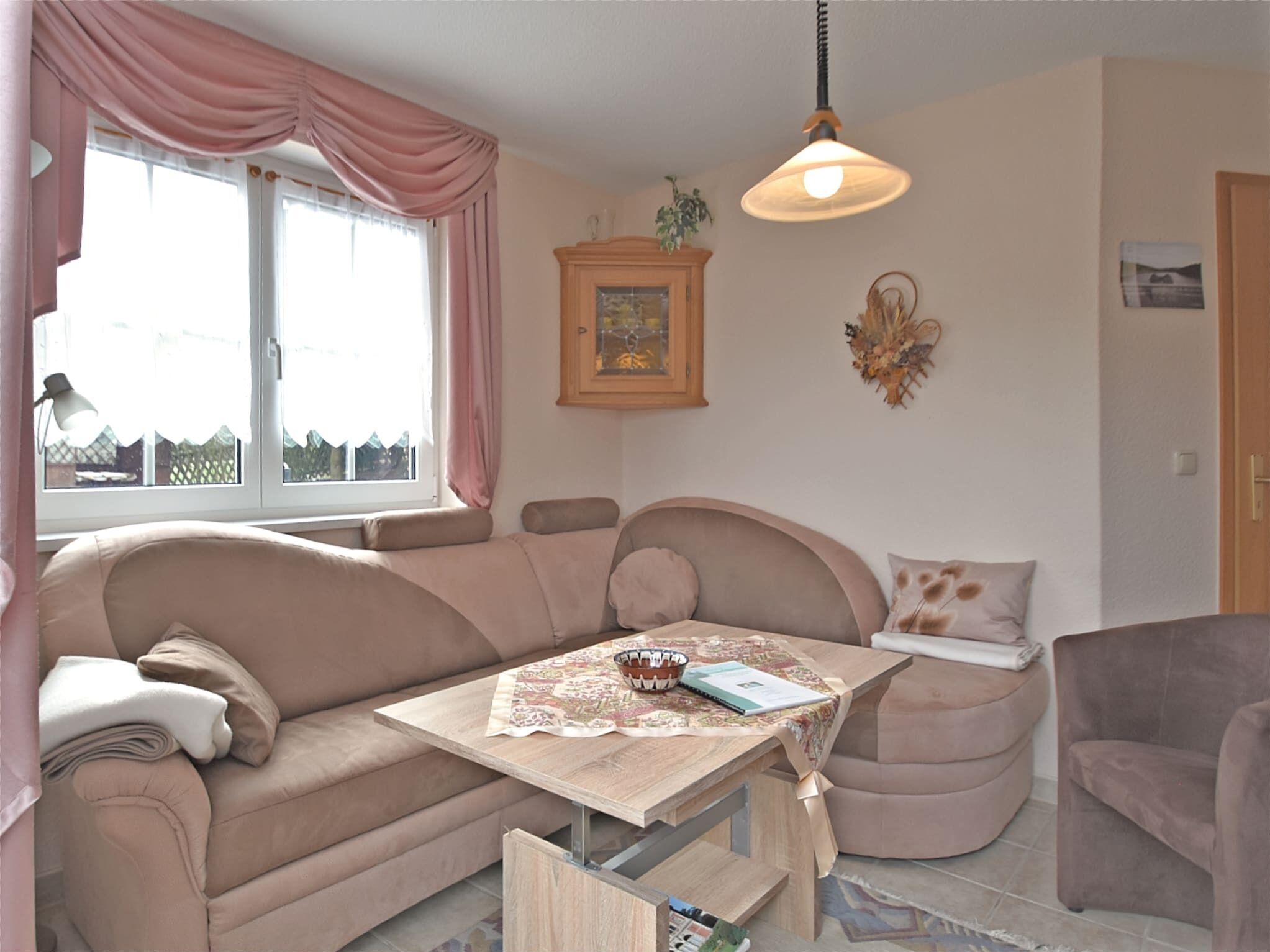 A cozy living room with a sofa, a small table, a lamp, and a window with curtains.
