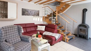 A modern living room with a red sofa, a plaid armchair, a glass coffee table, and a wooden staircase. - Comfortable holiday home in Saxony with terrace (Oederan)