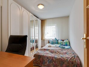 A bedroom with a bed, a chair, a wardrobe, and a window with curtains.