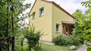 Une maison à deux étages, avec une façade jaune, un toit en briques et un petit porche à l’avant.
