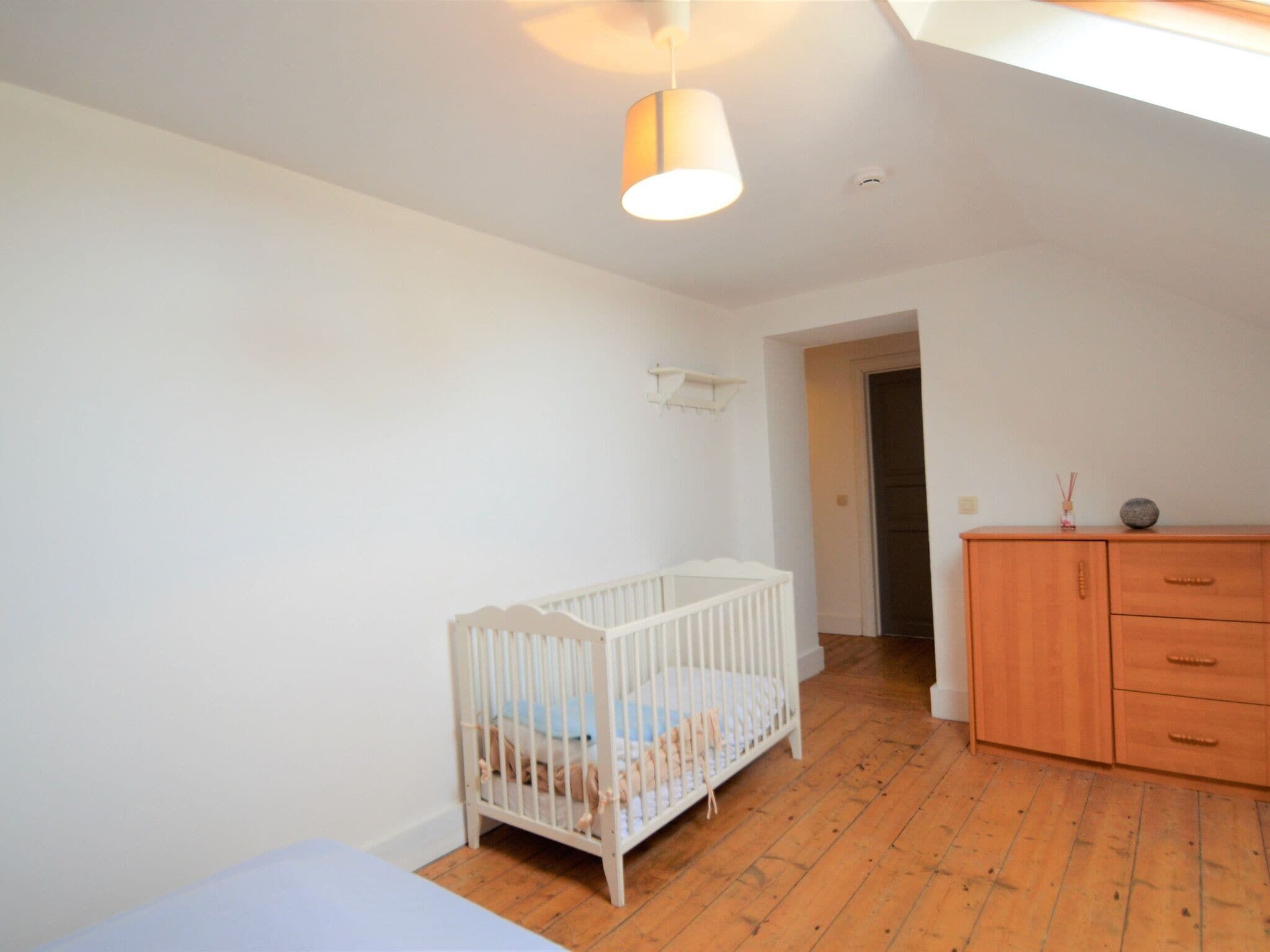 Une chambre avec un berceau blanc, une commode en bois et un luminaire suspendu.