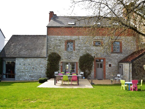 A stone building with a brick roof, a patio with colorful chairs, and a small garden area.