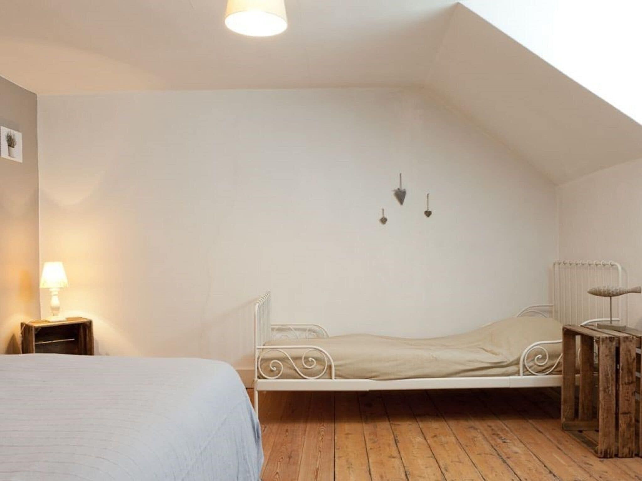 Habitación individual con techo inclinado, un radiador, una mesita de noche con lámpara y un taburete de madera pequeño.
