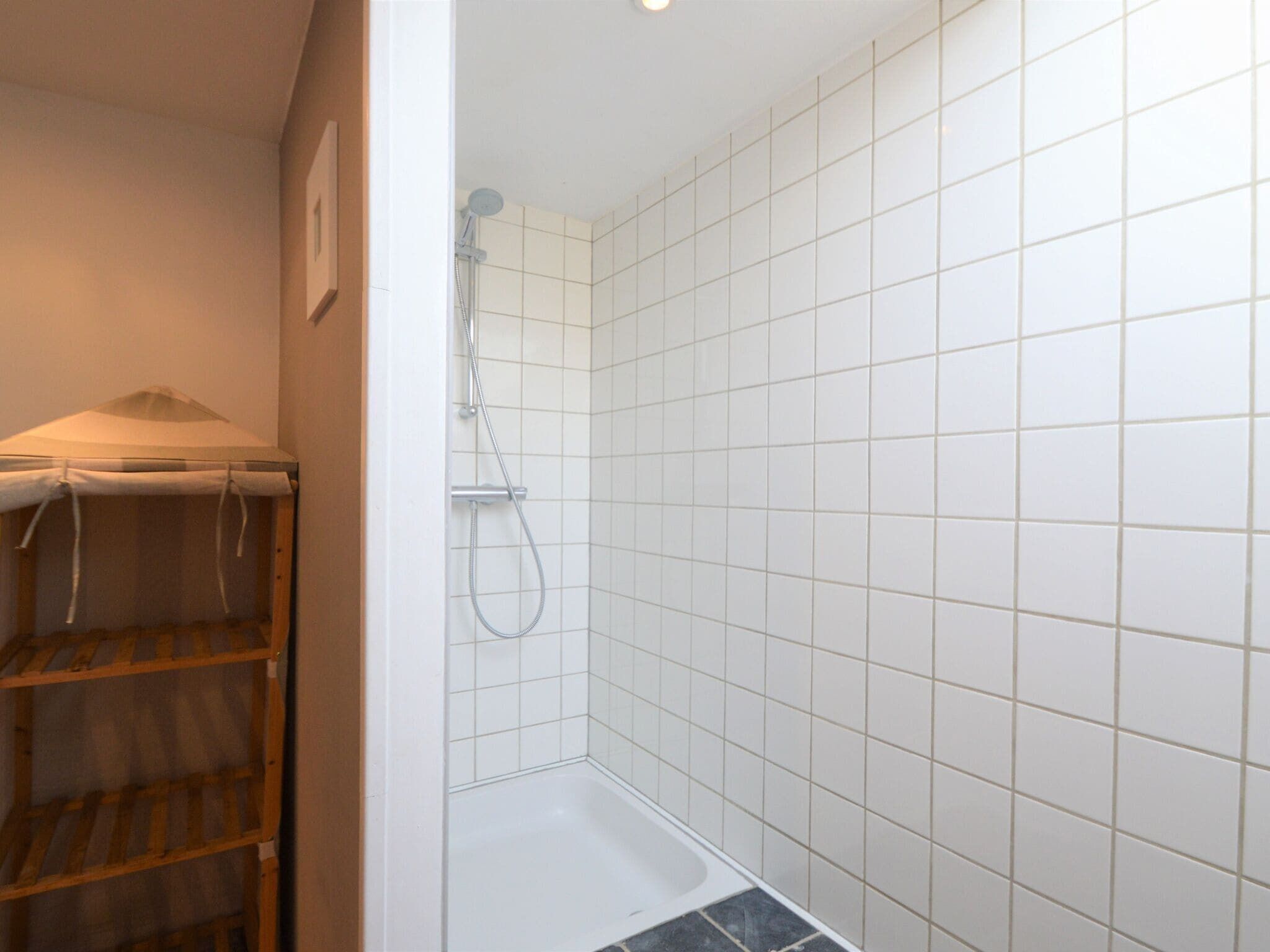 Un baño pequeño con azulejos, ducha y estante de madera.
