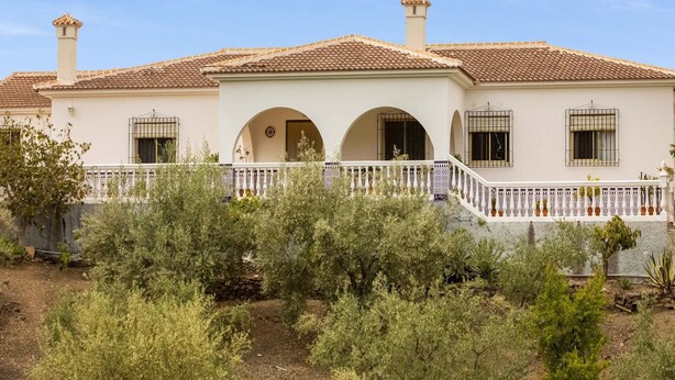 A two-story house with a tiled roof, white walls, and a white fence. There are two chimneys and a balcony with a railing. - Casa La Loma with Pool (Andalucía)