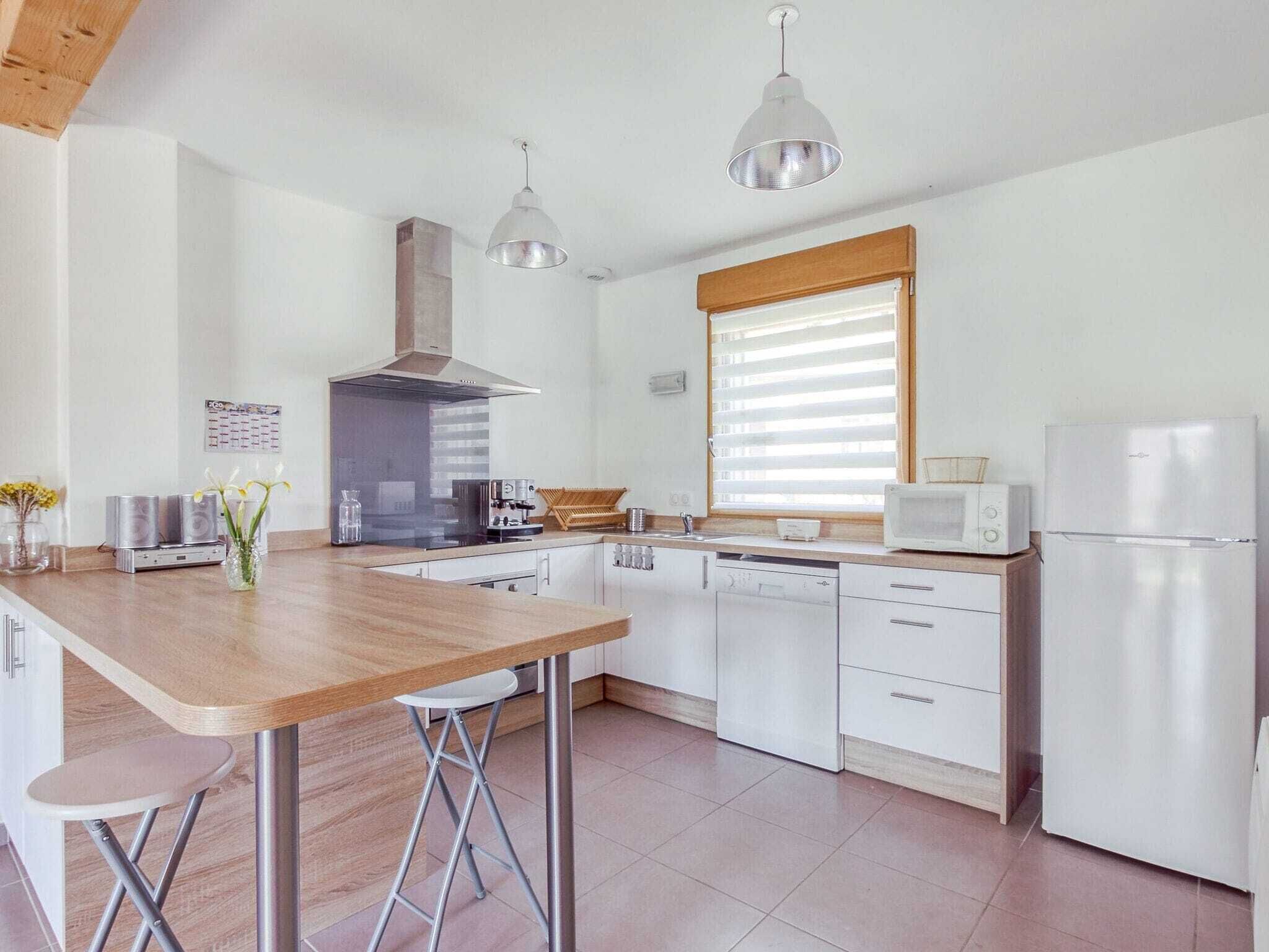 Una cocina moderna con barra de madera, electrodomésticos de acero inoxidable e iluminación colgante.