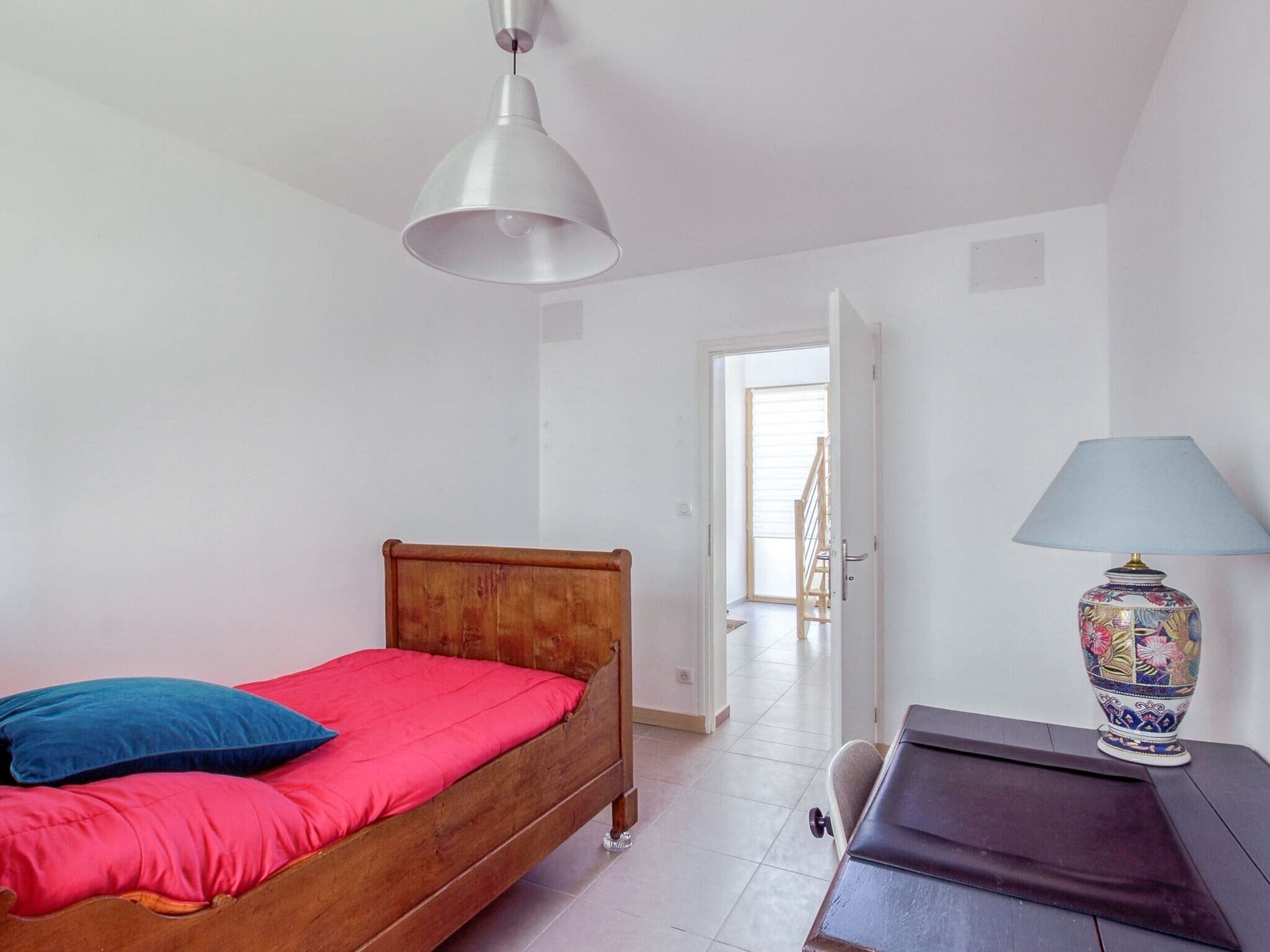 A bedroom with a wooden bed, a desk with a lamp, and a white ceiling light.