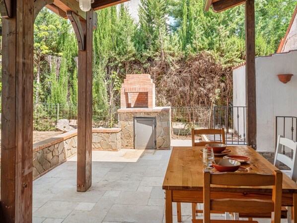 An outdoor patio with a stone fireplace, wooden table, and chairs.