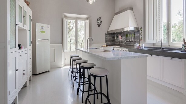 Cocina moderna con una isla central, taburetes de bar, un refrigerador y un ventanal grande que ofrece luz natural.