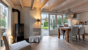 Ein modernes Wohnzimmer mit Kaminofen, einem Essbereich mit Stühlen und einer durchgehenden Tür einsehbarer Küche.