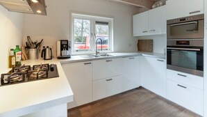 Eine moderne Küche mit weißen Schränken, einem Gasherd, einem Backofen und einem Fenster mit Blick nach draußen.