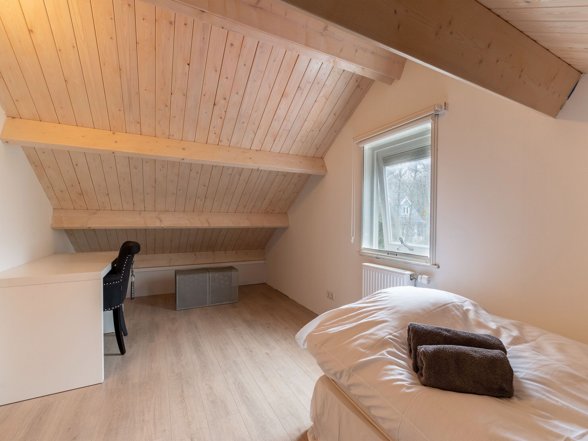 Ein Schlafzimmer mit schrägem Dach, einem Fenster, einem Heizkörper und einem Bett mit Kissen.