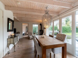 Un amplio comedor con una mesa y sillas de madera, una araña y ventanas grandes que ofrecen vistas al exterior.