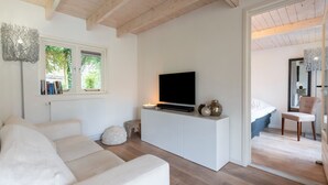 Ein modernes Wohnzimmer mit einem weißen Sofa, einem Fernseher auf einem weißen Schrank und einem Fenster mit Büchern auf der Fensterbank.