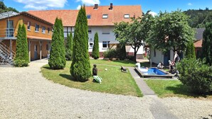 A courtyard with a swimming pool, neatly trimmed hedges, and a building with a red-tiled roof. - Wohnung in Huddingen mit Terrasse (Bad Wildungen)