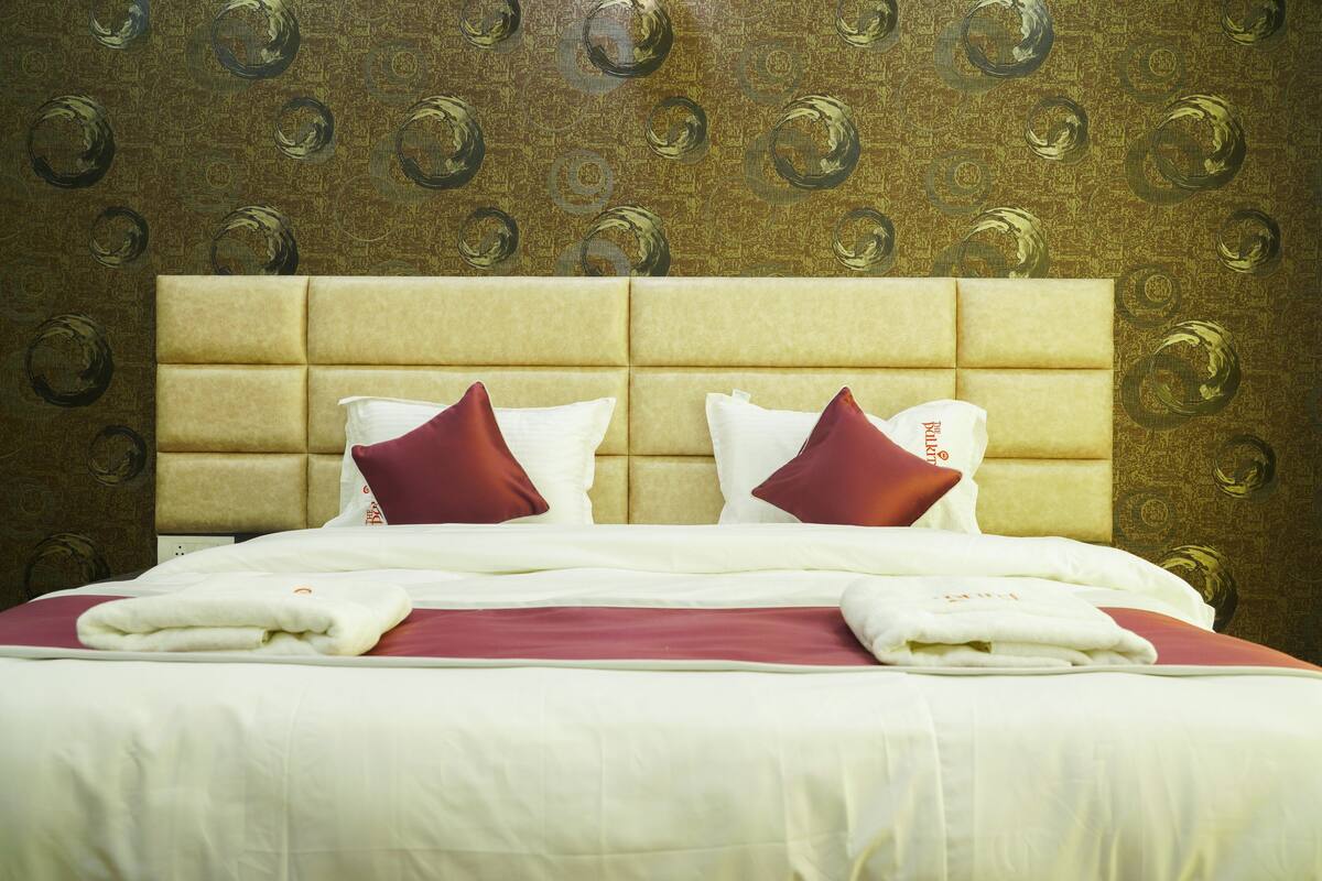 A hotel room with a large bed, a headboard, and a patterned wallpaper.