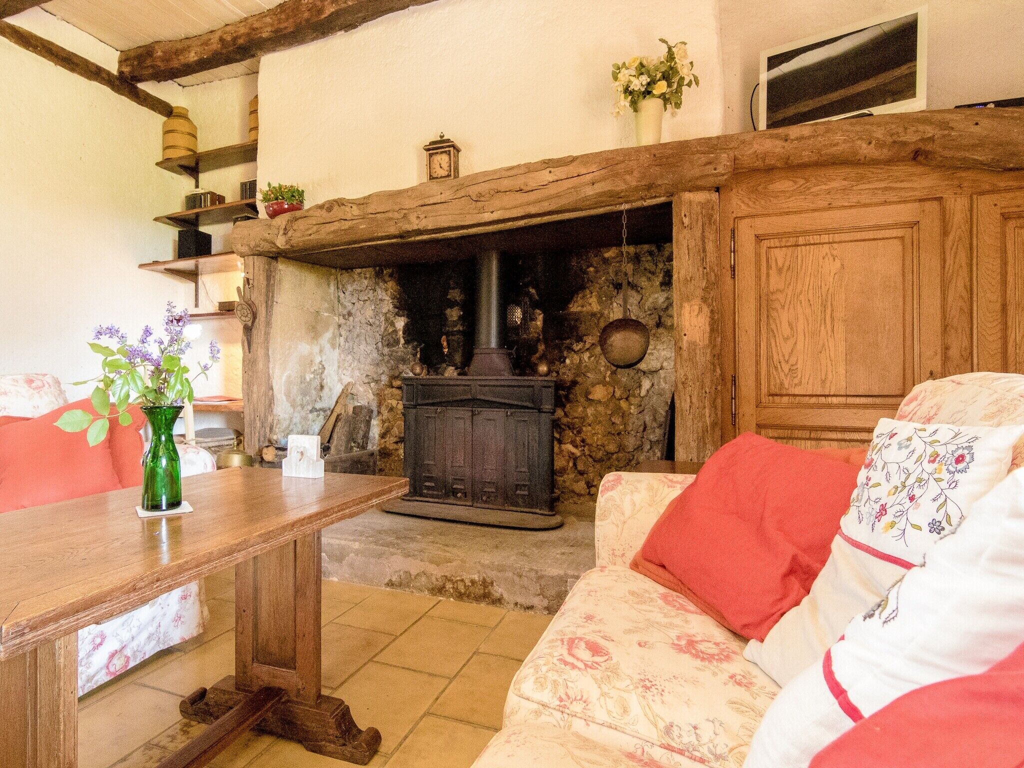 A cozy living room with a stone fireplace, wooden furniture, and a floral-patterned sofa.