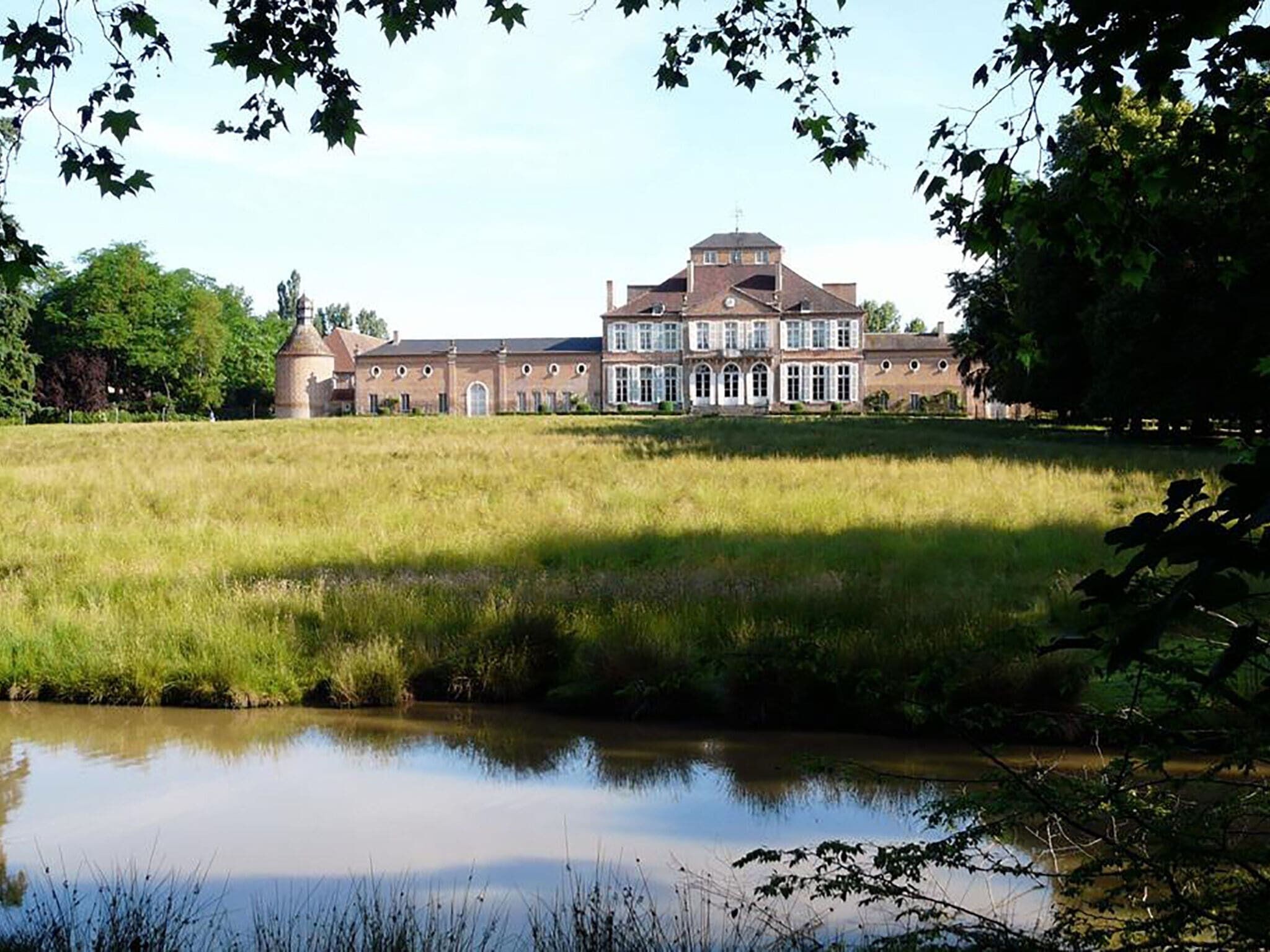 A large, historic building with a symmetrical facade, a central tower, and a surrounding grassy field.