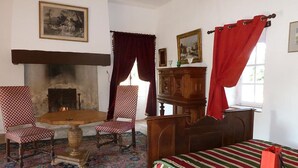 A traditional room with a fireplace, a bed with a striped bedspread, two armchairs, and a wooden cabinet. - Outbuilding of a listed 16th-century château (Château-sur-Allier)