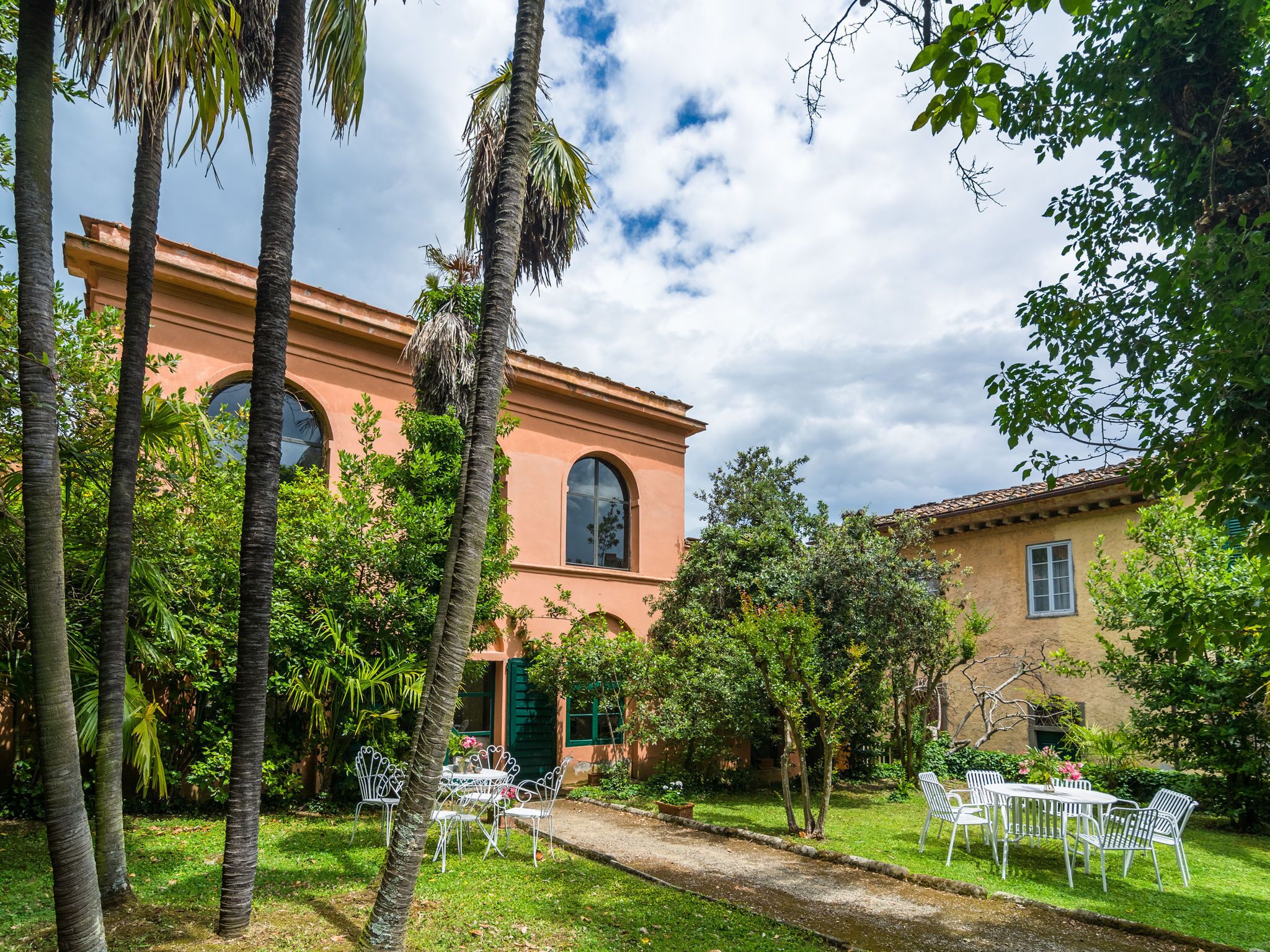 A building with a pink facade, surrounded by lush greenery and palm trees.