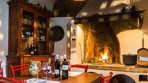 Un comedor rústico con una mesa de madera, sillas rojas, un aparador con botellas y una chimenea con leña.