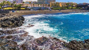 A coastal hotel with a beach view, rocky shoreline, and multiple buildings in the background.