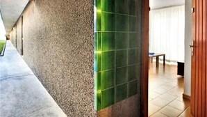 A hallway with a textured wall, a green-tiled column, and a wooden door leading to a room with a tiled floor.