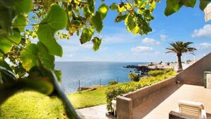 A coastal property with a view of the sea, a paved patio, and a small garden area.