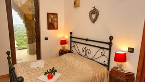 Un dormitorio con cama, dos mesitas de noche, una lámpara roja, un adorno en la pared y vistas a través de una puerta abierta.