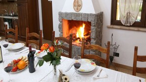Un comedor con chimenea de piedra, sillas de madera, una mesa dispuesta con platos, copas de vino y una botella.