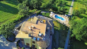 Vista aérea de una propiedad con piscina, un patio con mobiliario exterior y un edificio curvo con tejado de baldosas.
