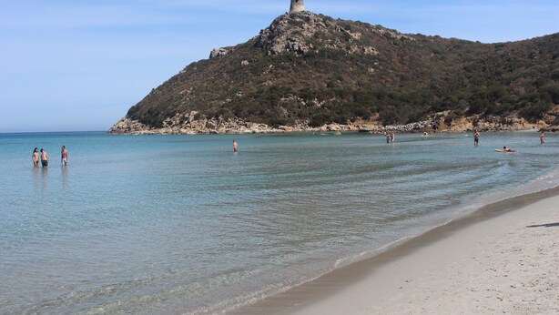 A beach with clear water, a sandy shore, and a hill with a tower. - Picturesque flat with sea view (Geremeas Quartu Sant'elena)