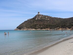 A beach with clear water, a sandy shore, and a hill with a tower.