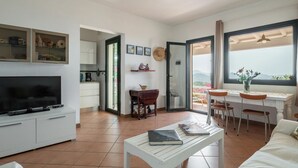A spacious living room with a flat-screen TV, a dining area with a table and chairs, a kitchen with cabinets and a coffee machine, and a balcony with a view. - Picturesque flat with sea view (Geremeas Quartu Sant'elena)