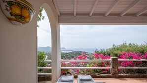 A terrace with two lounge chairs, a decorative wall piece, and a view of the sea and hills. - Picturesque flat with sea view (Geremeas Quartu Sant'elena)