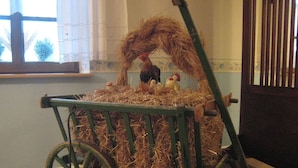 A rustic chicken coop with a wheelbarrow, straw bedding, and a rooster and chicks.