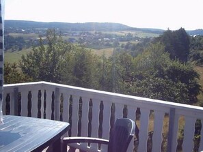 Ein Balkon mit Tisch und Stühlen mit Blick auf eine ländliche Landschaft mit Feldern und Bäumen.