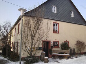 Ein zweistöckiges Haus mit geneigtem Dach, einer Veranda mit einer Bank und einem Briefkasten.