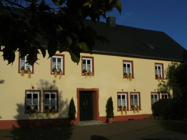 Ein zweigeschossiges Gebäude mit einer gelben Fassade, zahlreichen Fenstern mit roten Rahmen und Blumentöpfen im Erdgeschoss.