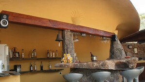 A bar area with a curved yellow wall, wooden beam ceiling, stone pillars, and bar stools.