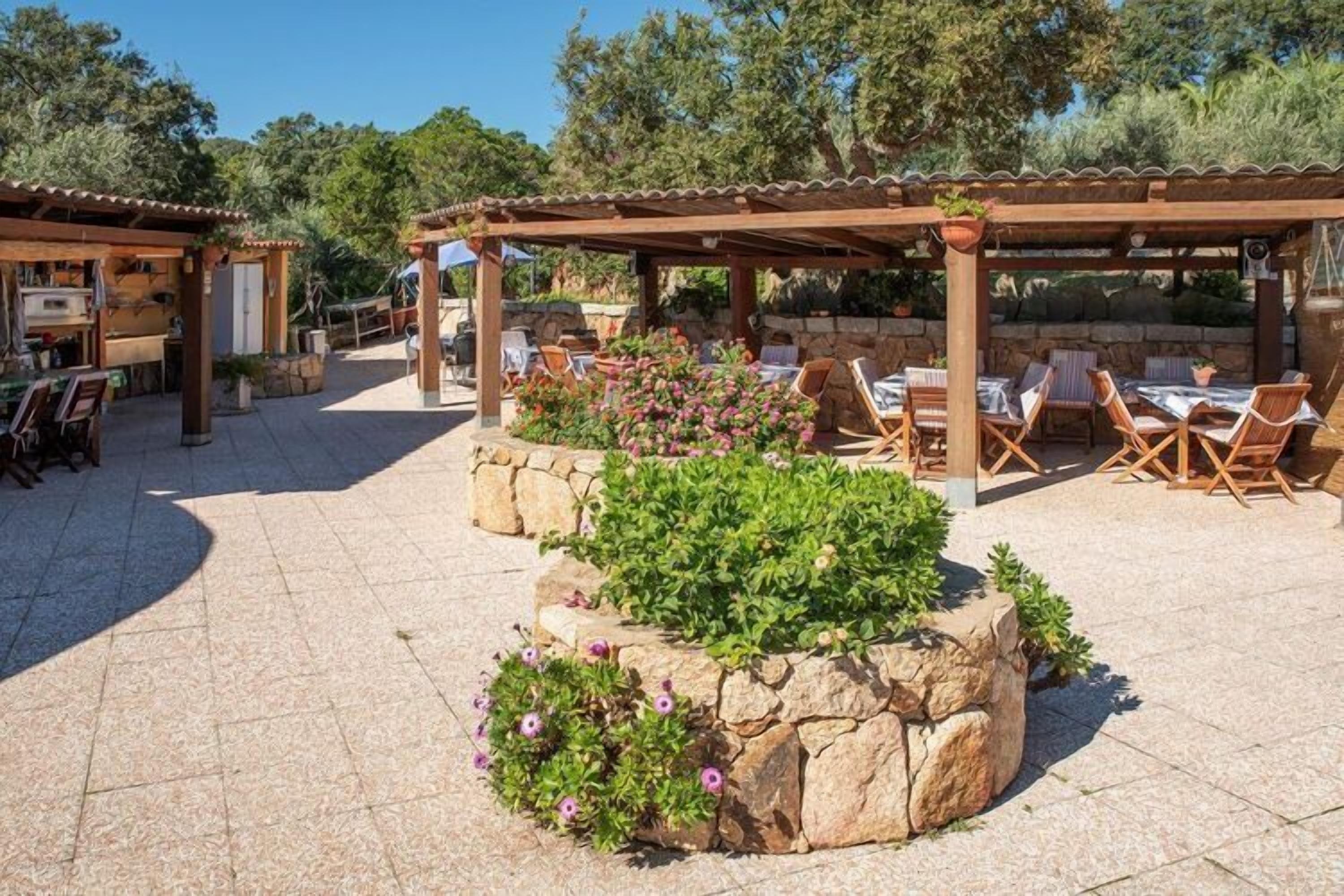 An outdoor patio area with stone planters, wooden tables, and chairs.
