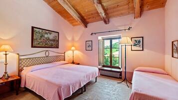A bedroom with two beds, a wooden ceiling, a window with a view, and a painting on the wall.