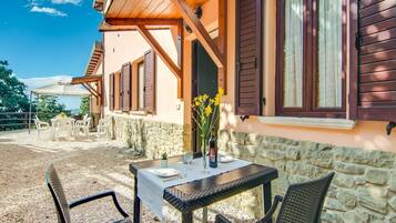 A rustic outdoor seating area with a table and chairs, a stone wall, and wooden shutters.