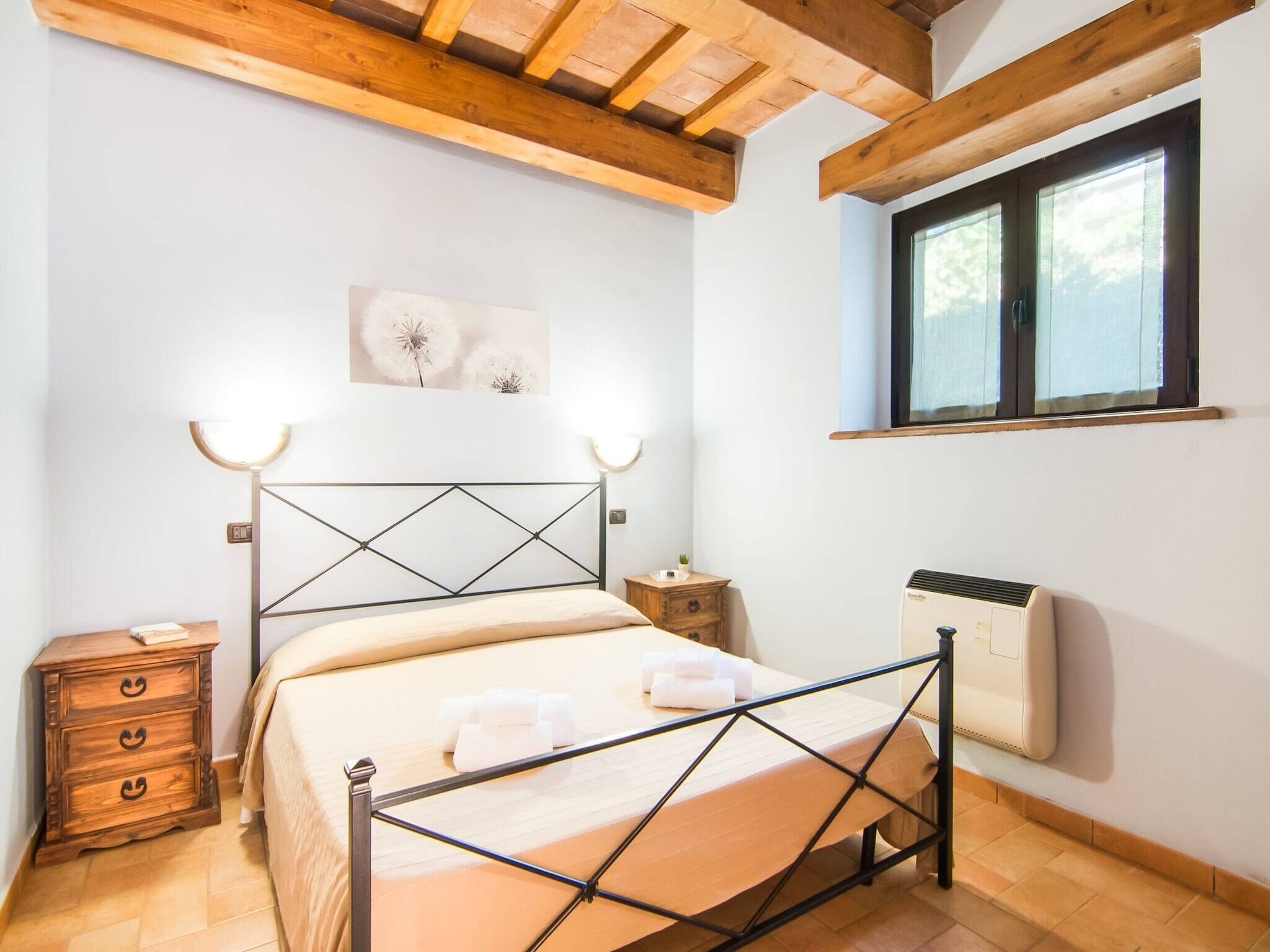 A bedroom with a bed, bedside tables, a radiator, and a window.