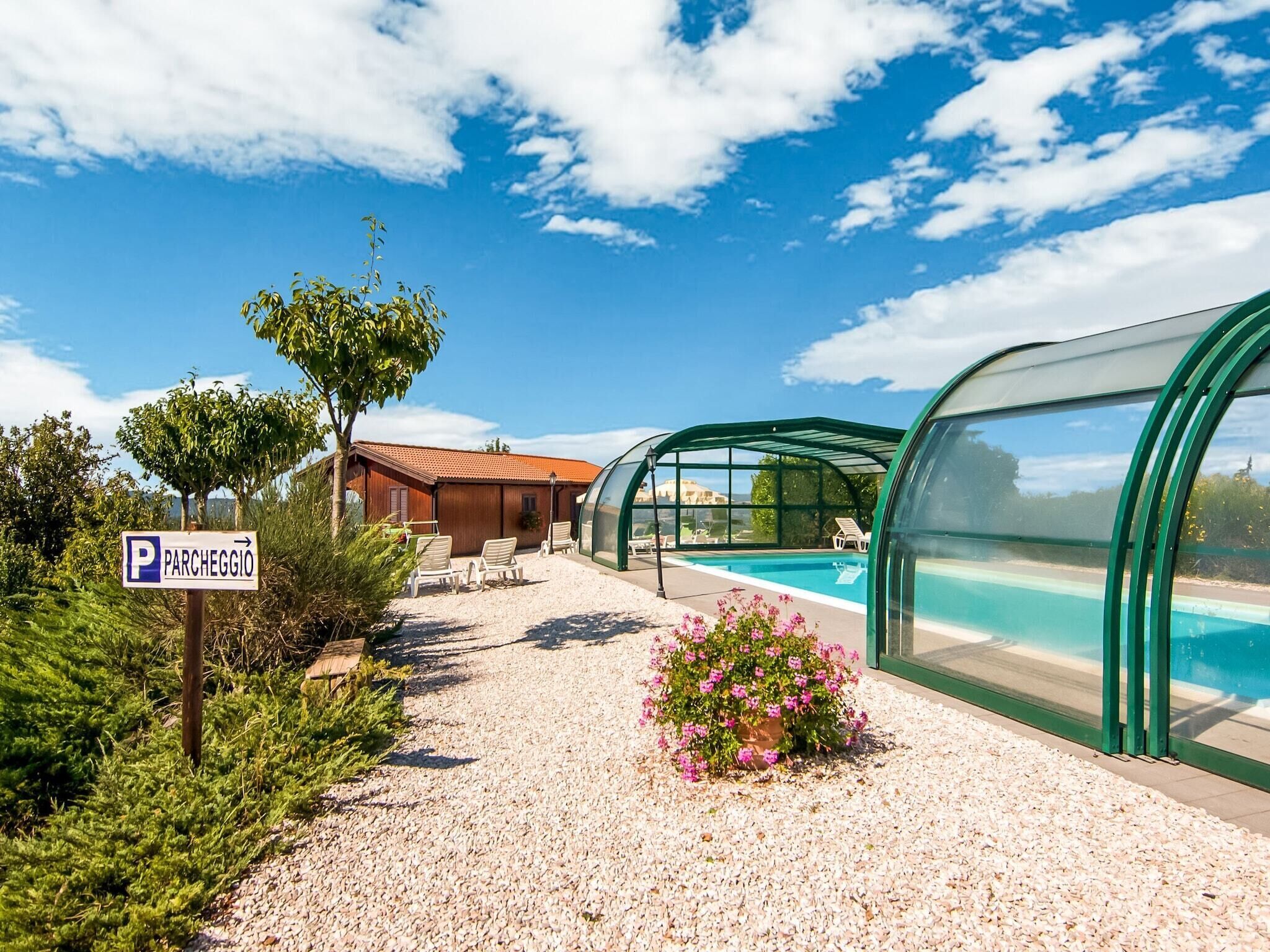 A pool area with a covered seating area, a sign for 'Parchèggio', and a gravel path.