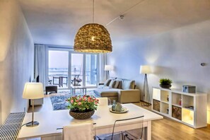A modern living room with a white sofa, a dining table with a bowl of flowers, and a hanging light fixture. - Modern Apartment in Den Haag (Den Haag)